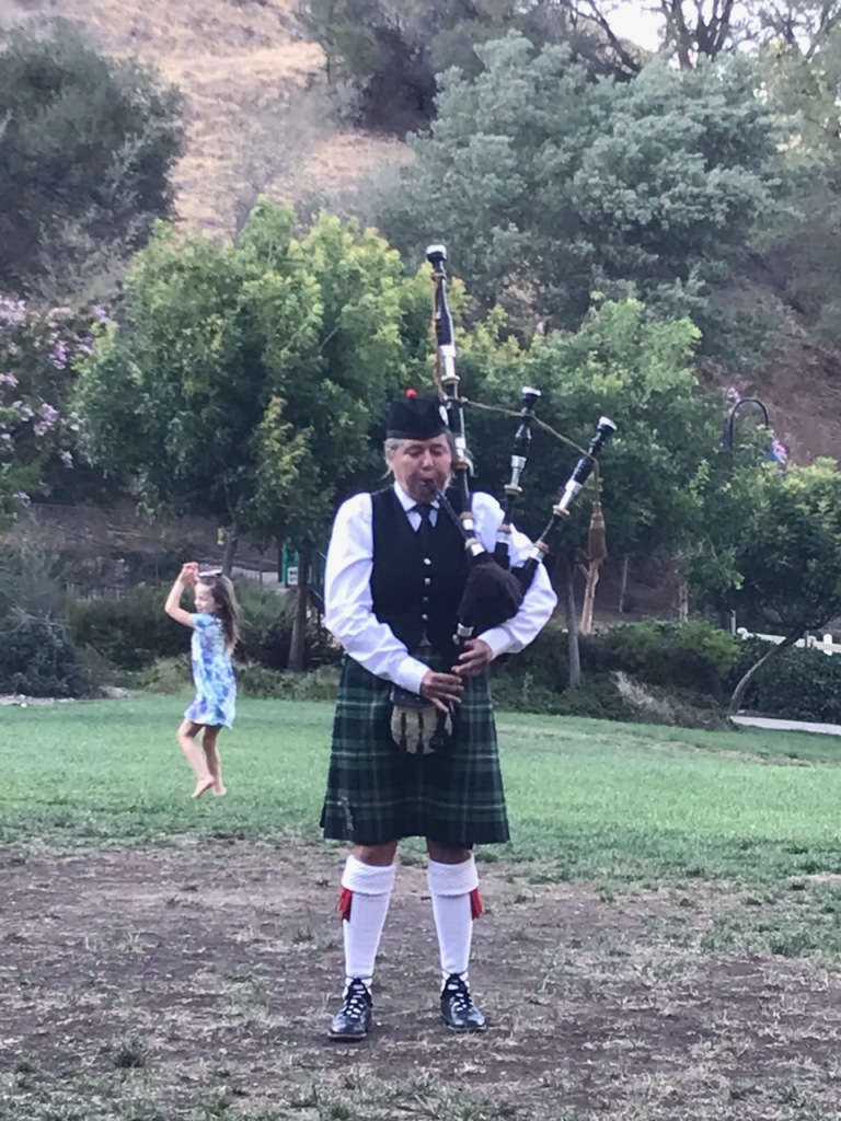 Elise in Martinez, California, playing bagpipes with a young child dancing to the music.
